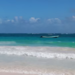 Peaceful Tulum beach scene featuring a boat on turquoise waters under a clear blue sky.